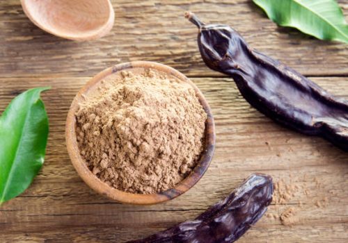 Carob pods and carob powder over wooden background with copy space - organic healthy ingredient for vegan vegetarian food and drinks